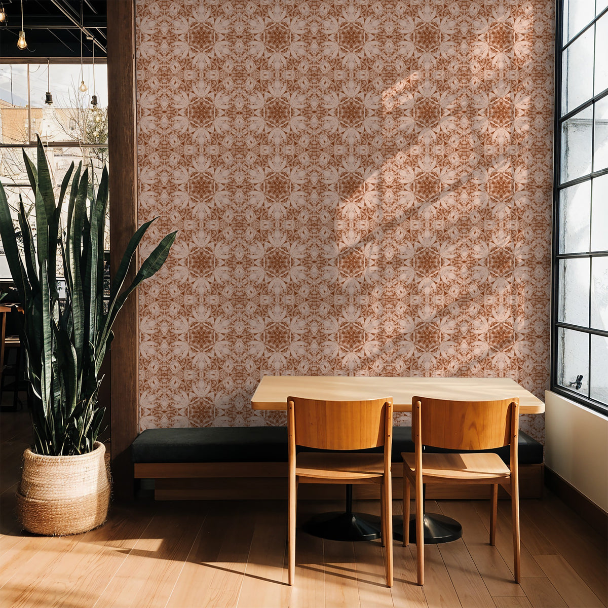 Terracotta and cream kaleidoscopic wallpaper in sunlit cafe setting with wooden chairs.